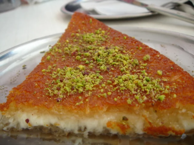 Üzerinde eriyen peynir ve fıstıkla servis edilmiş künefe dilimi